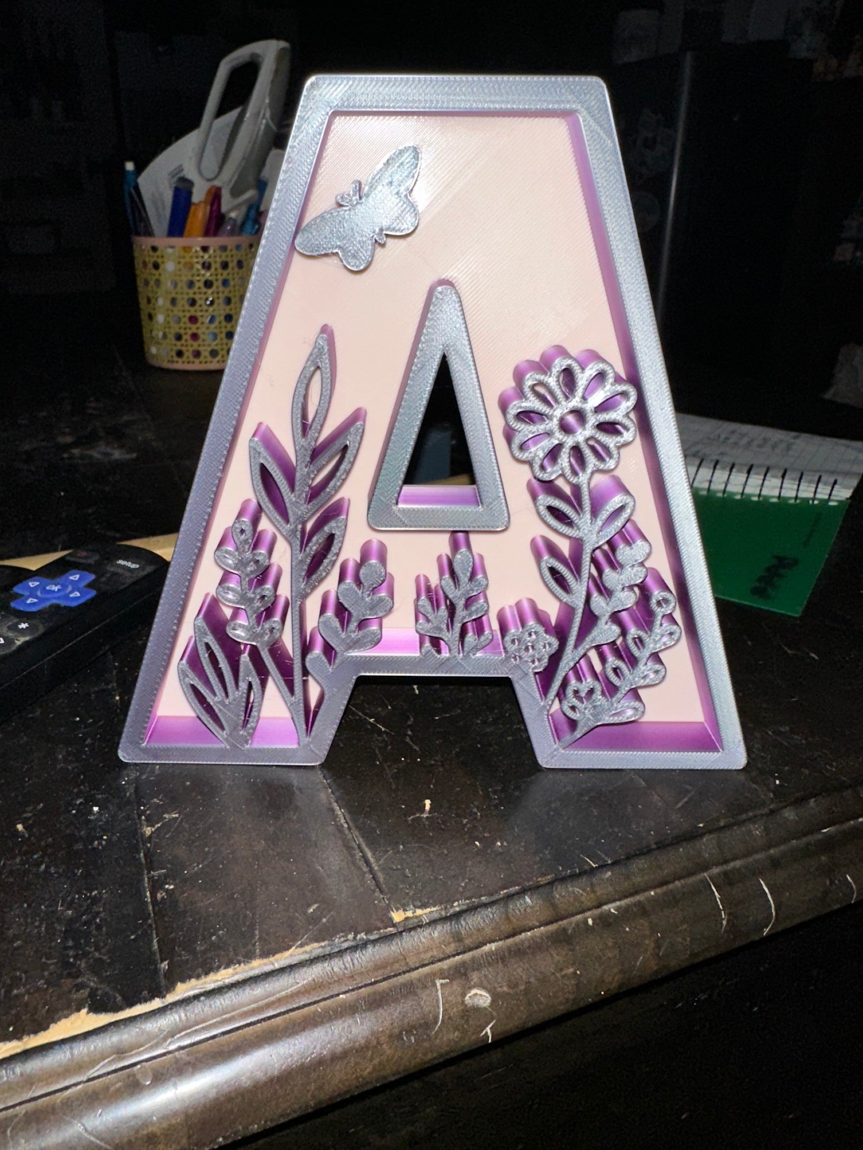 Papa Tee's decorative 3D printed letter A with silver floral and butterfly accents on a pink background with a silver border.