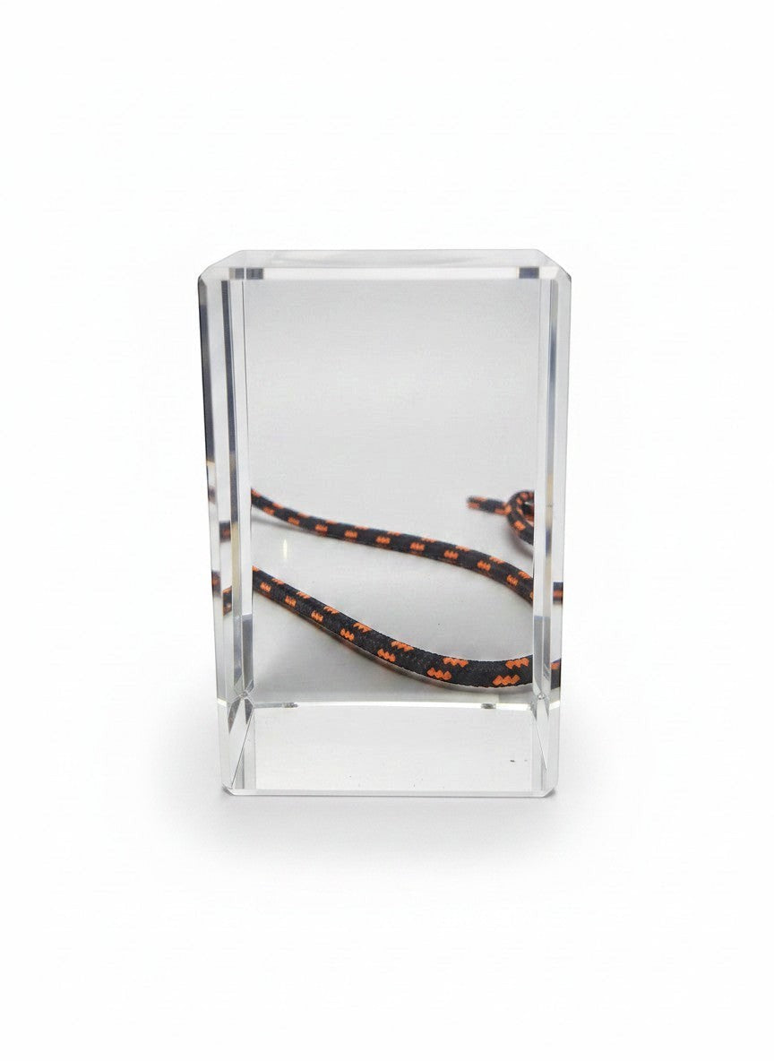 Papa Tee's black and orange patterned rope displayed inside a clear acrylic block.